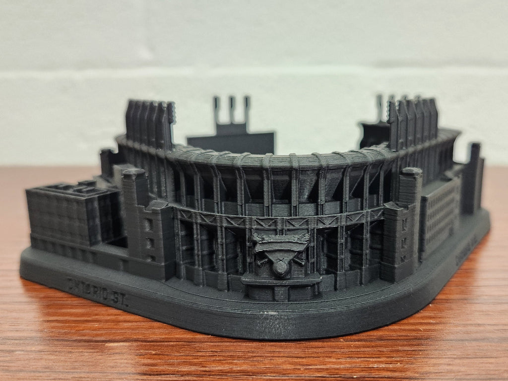 Black 3D-printed model of a stadium on a wooden surface with a white background