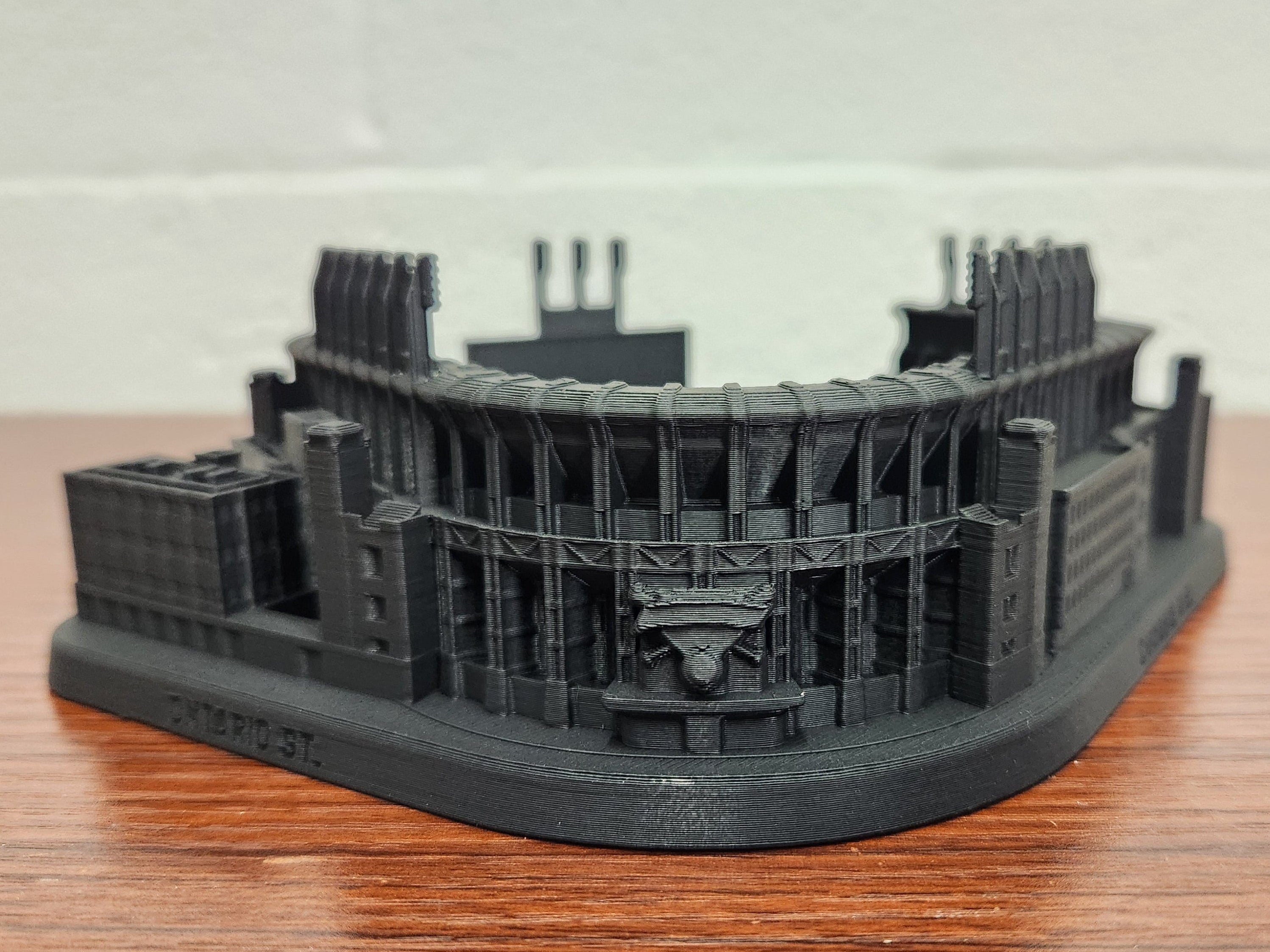 Black 3D-printed model of a stadium on a wooden surface with a white background